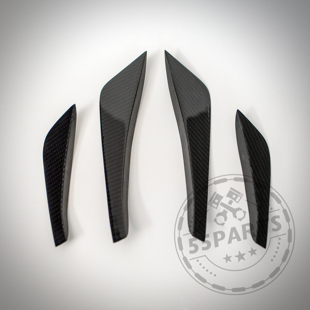 Vier 55Parts Echtcarbon Canards passend für BMW F82/F83 M4 & M4 CS, hergestellt aus echter Kohlefaser, dargestellt auf einer weißen Oberfläche mit einem schwachen Logo-Wasserzeichen.