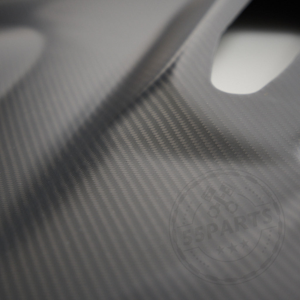 Nahaufnahme der strukturierten Kohlefaser, dezent beleuchtet, hebt 55Parts Carbon Türverkleidung Türpappen passend für BMW F2x 1er/2er und F87 M2/M2 Competition/M2 CS hervor. In der Ecke erscheint ein schwaches kreisförmiges Logo.