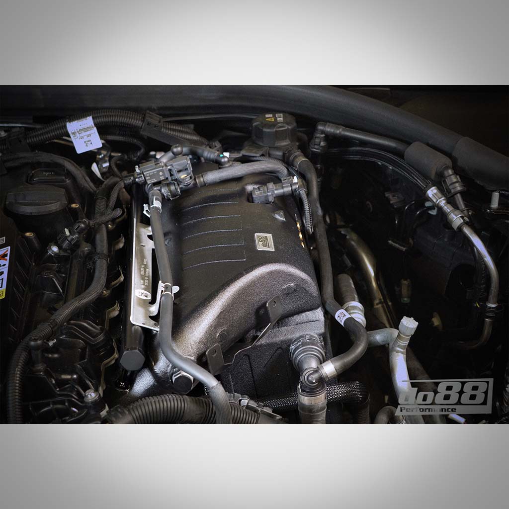 Nahaufnahme eines Automotorraums mit hervorgehobenen Tuningelementen des do88 S58, einschließlich der DO88-Ansaugbrücke mit integriertem Ladeluftkühler für G87 M2, G80/G81 M3 und G82/G83 M4.