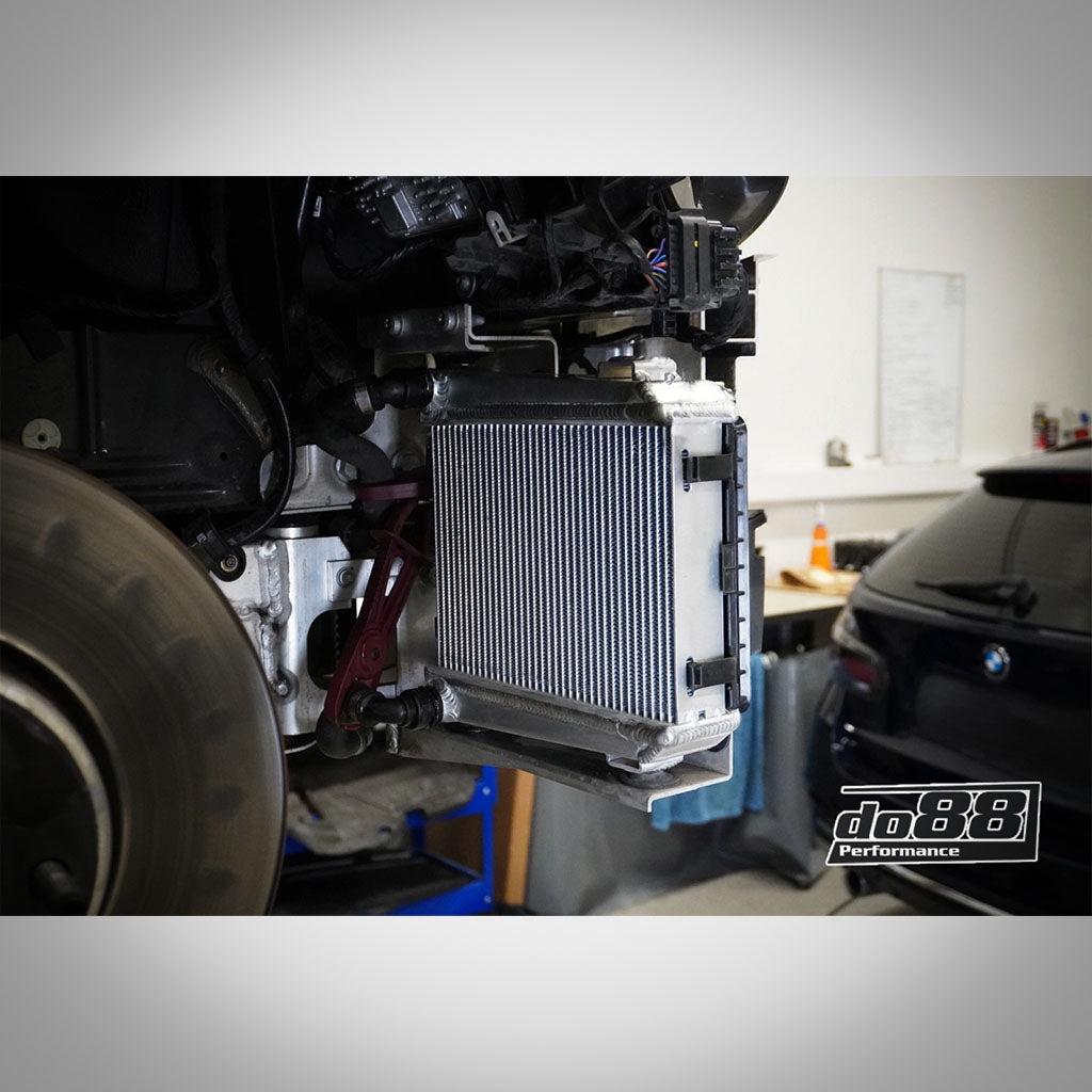 Eine Nahaufnahme eines do88 Aluminium Upgrade Kühlmittelkühlers, passend für BMW G42 M240i, G2X M340i/M440i, G29 Z4 M40i und Toyota Supra MK5 A90, installiert im Radhaus eines Autos mit B58 Motor in einer Garage.