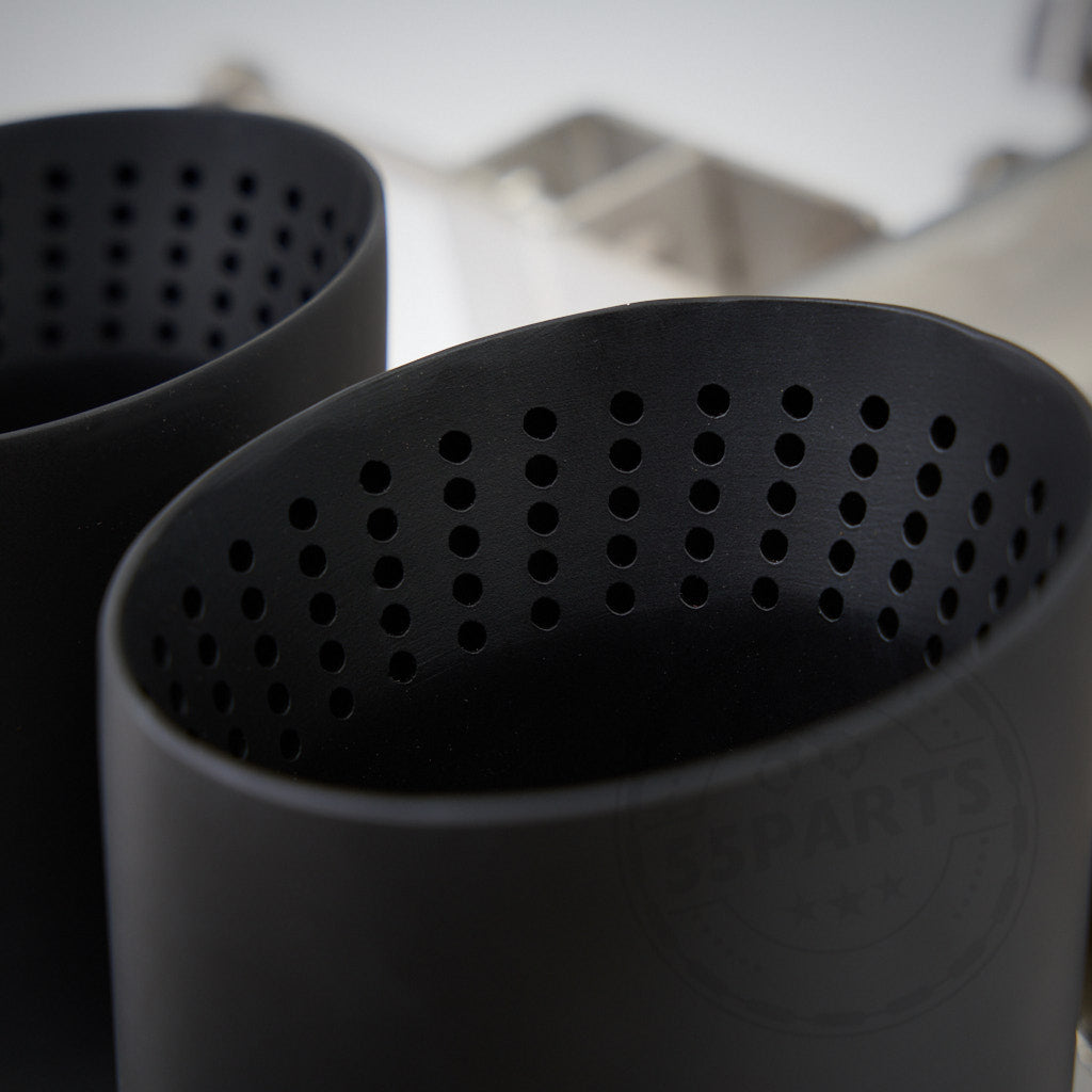 Nahaufnahme von zwei schwarzen, perforierten Zylindern der 55Parts Special 3" ECE Abgasanlage passend für BMW G8x Modelle (G81, G82, G83, G87 M2/M3/M4 mit S58 Motor), vor unscharfem Hintergrund.