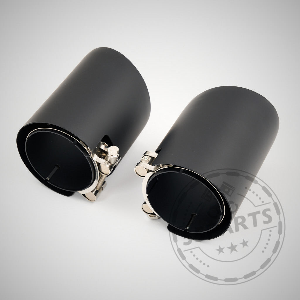 Zwei schwarze zylindrische Metall-Auspuffblenden mit silbernen Klemmen & MH-PIPES für alle B58 BMW-Modelle (OHNE OPF & OPF) inkl. Toyota Supra, aus dem 55Parts SPECIAL: 3,5" ECE-Klappenauspuffanlage, auf hellgrauem Hintergrund.