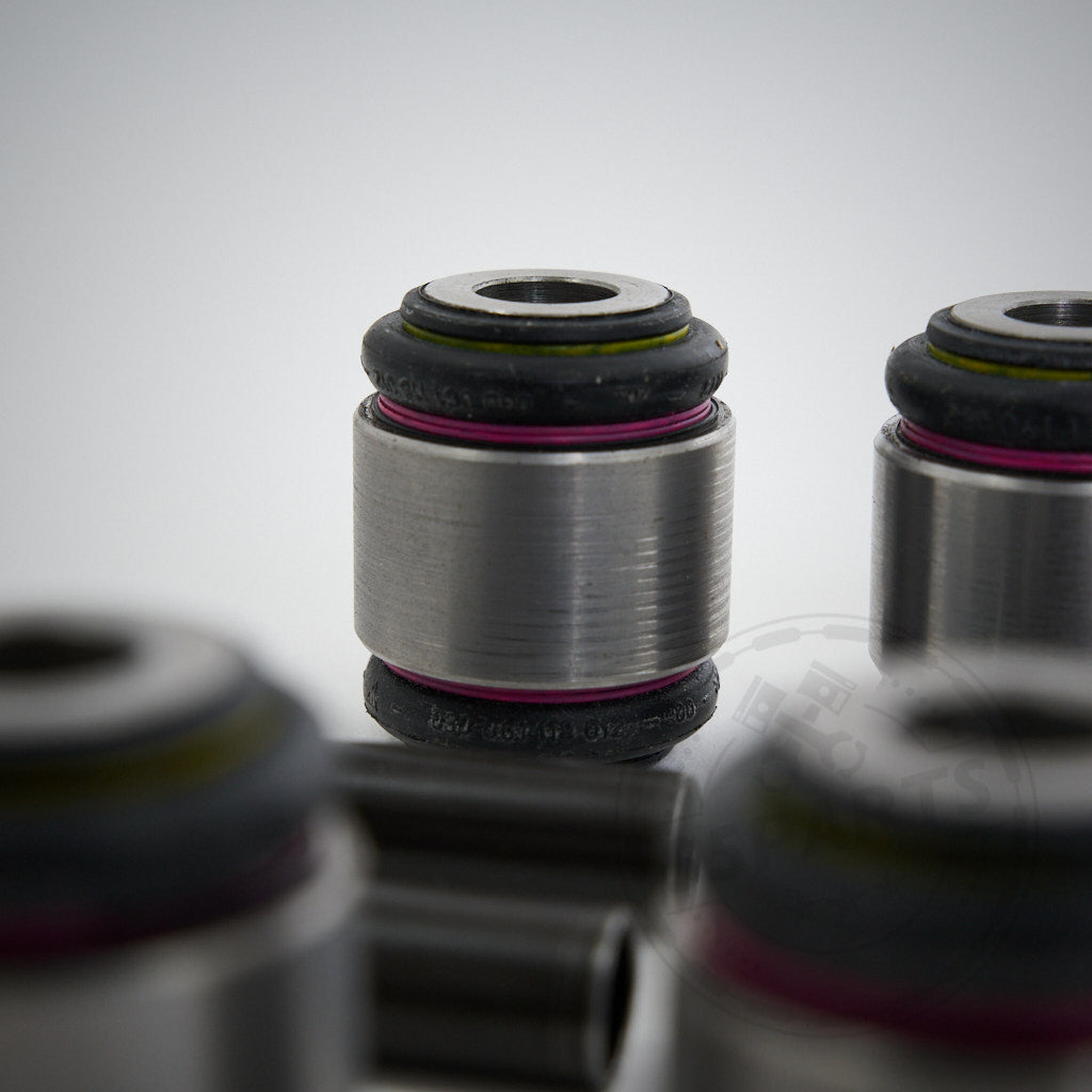 Nahaufnahme der zylindrischen NoFlex-Lager aus Metall für originale obere Querlenkergelenksätze, entwickelt für die BMW F8x- und G8x-M-Modelle, mit schwarzen und rosa Ringen auf hellem Hintergrund.