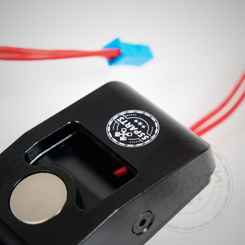 Nahaufnahme einer schwarzen 55Parts Special: V2 magnetischen Schaltwippe mit rundem Magneten und roten Kabeln, versehen mit dem 55Parts-Logo. Passend für fast alle BMW und MINI Modelle der F- und G-Serie mit Plug-and-Play-Montage.