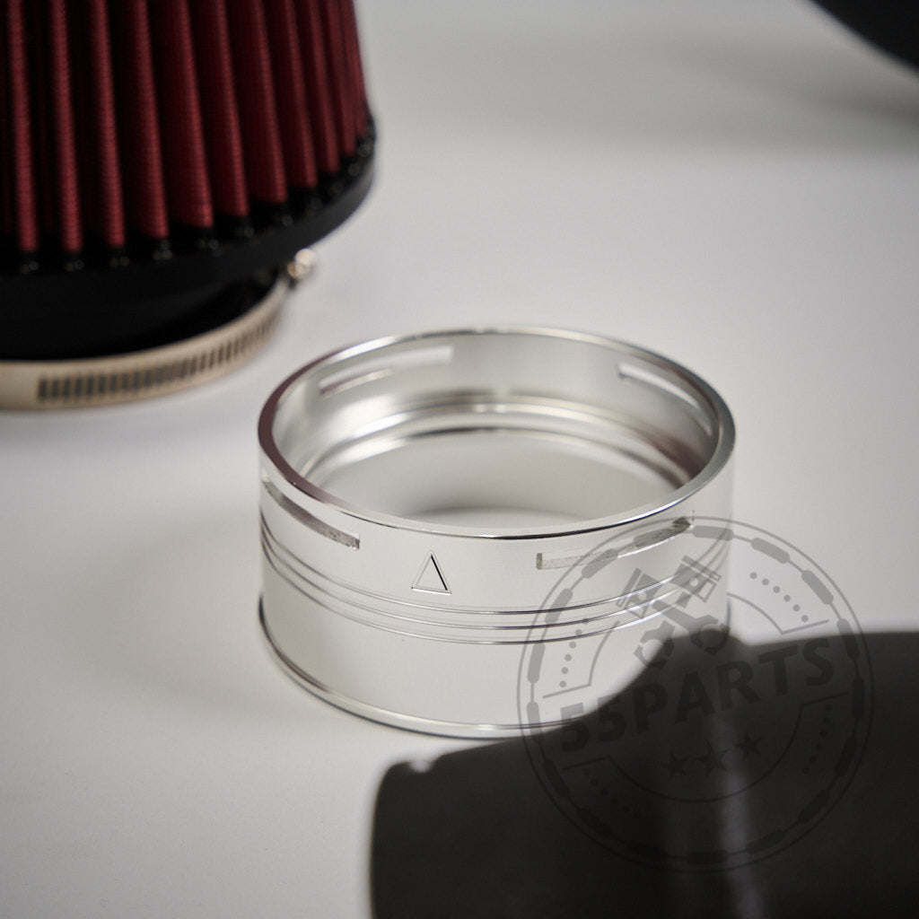 Silbernes Autoteil aus Metall mit eingraviertem Dreieck, abgebildet neben einem roten Luftfilter – perfekt für die Aufrüstung Ihres BMW G87 M2, G80/G81 M3 oder G82/G83 M4 S58 mit dem 55Parts Ansaugsystem Dual Cone Intake.