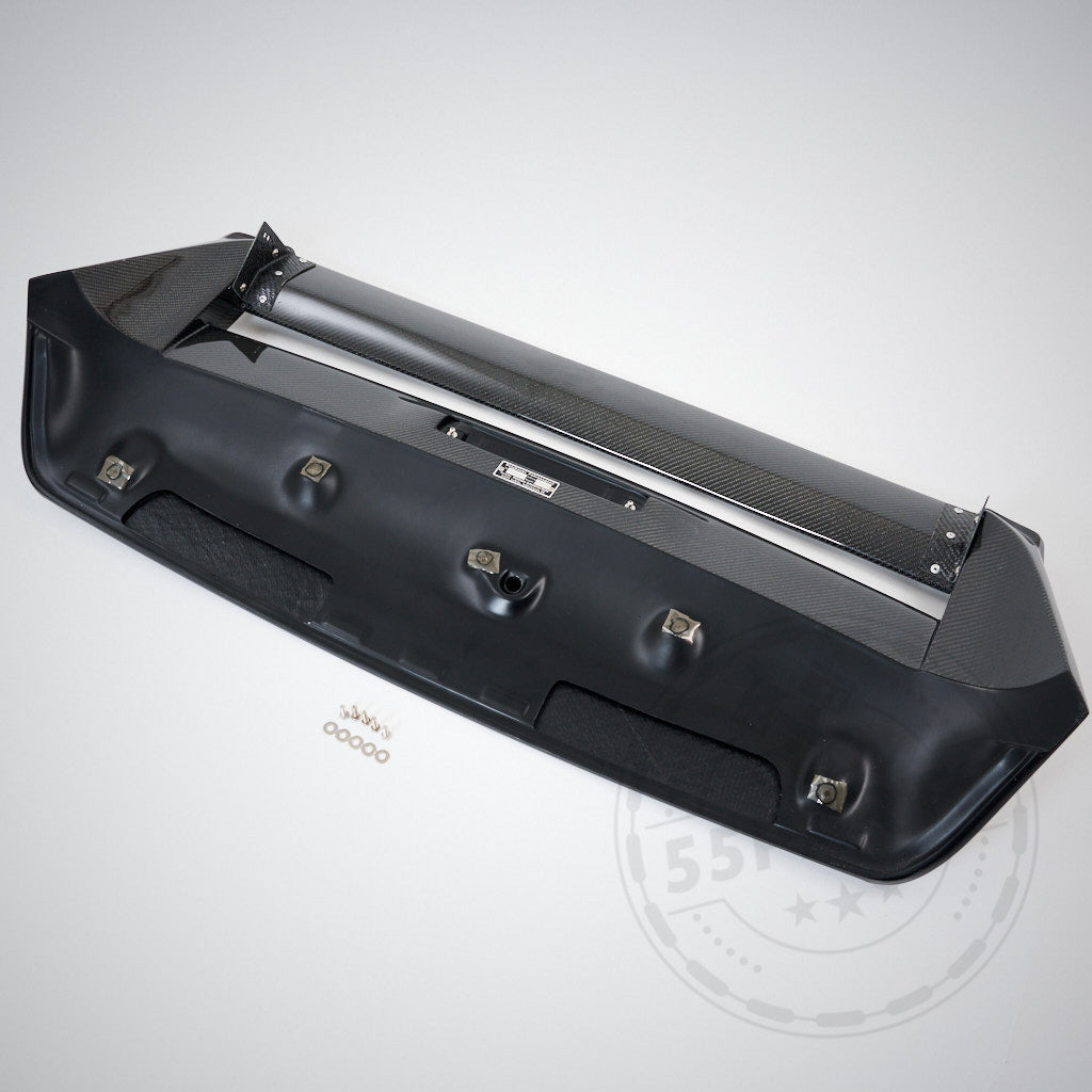 Der 55Parts Carbon Heckspoiler Heckflügel Verstellbar mit Teilegutachten, passend für Toyota GR Yaris (inkl. Facelift), wird mit Carbonfaserdetails und Montagematerial geliefert, dargestellt auf hellgrauem Hintergrund.