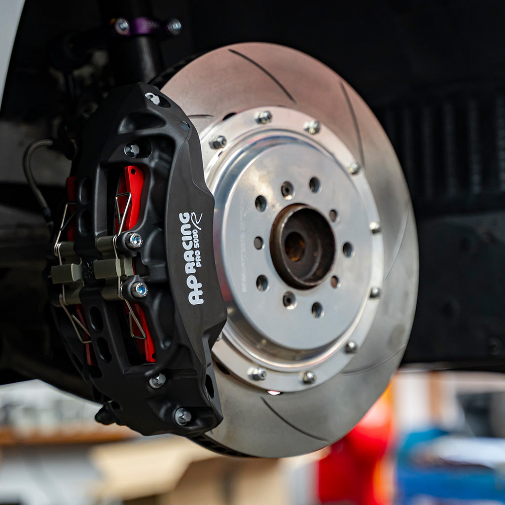 Nahaufnahme der Hochleistungsbremsscheibe und des Bremssattels von AP Racing eines Autos, die fortschrittliche Technik demonstrieren.