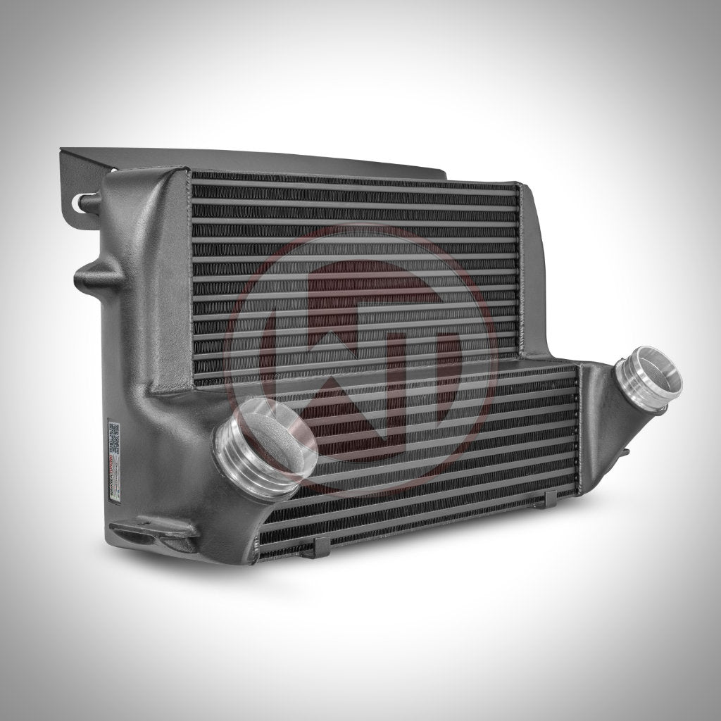 Der Wagner Tuning Evo 3 Competition Ladeluftkühler passend für BMW F2x, F87 N55 verfügt über doppelt abgewinkelte Einlass-/Auslassrohre, die auf einem Hintergrund mit Farbverlauf dargestellt sind – perfekt für Ihr BMW M135i/M235i FBO-Setup.