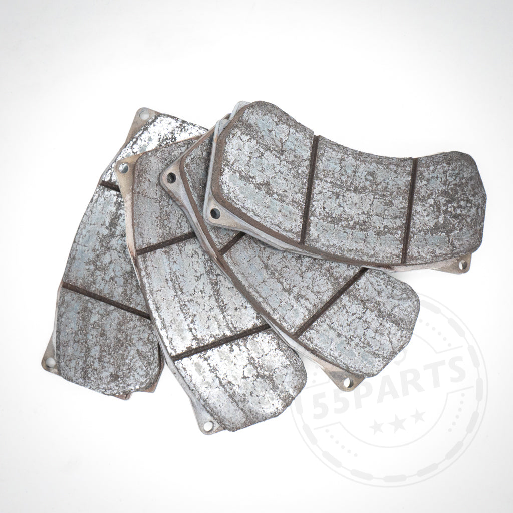 Vier gebrauchte 55Parts Special: AP Racing ST45 Bremsbeläge passend für CP9660 Bremssattel Bremsbeläge gestapelt auf einer weißen Oberfläche, mit starker Abnutzung und sichtbaren Kratzern.
