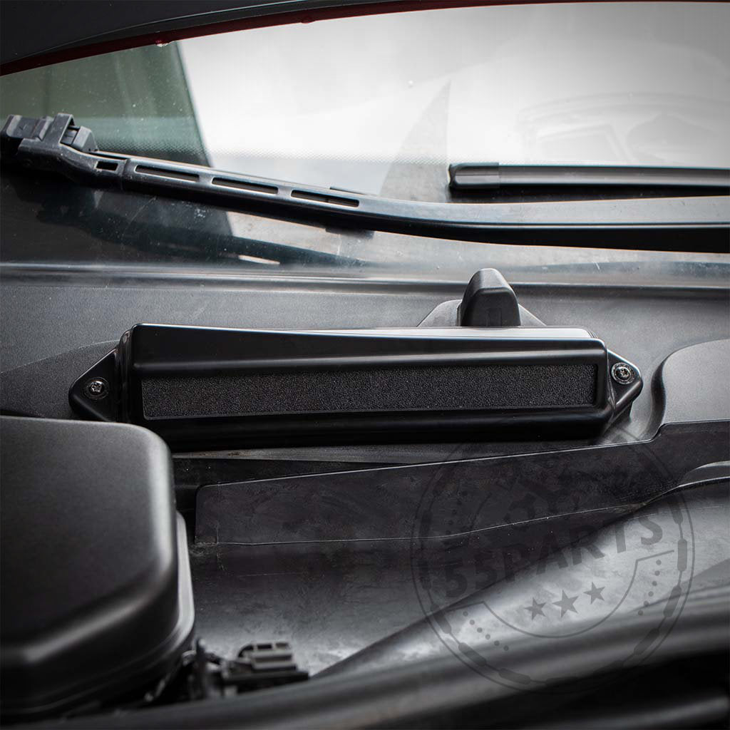 Nahaufnahme eines schwarzen 55Parts-Exklusiv: Bannik Engineering Mikrofilter-Löschgehäuses für die BMW E8x/E9x 1/3er-Serie, installiert an der Basis einer Windschutzscheibe mit sichtbarem Scheibenwischer.