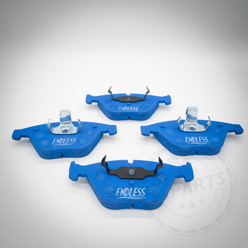 Vier blaue Endless Bremsbeläge für 1-Kolben Schwimmsattel passend für BMW 1er M Coupe, M3, E9x 325d-335i sind auf einer weißen Fläche mit einem schwachen kreisförmigen Logo im Hintergrund angeordnet, perfekt für Trackdays.