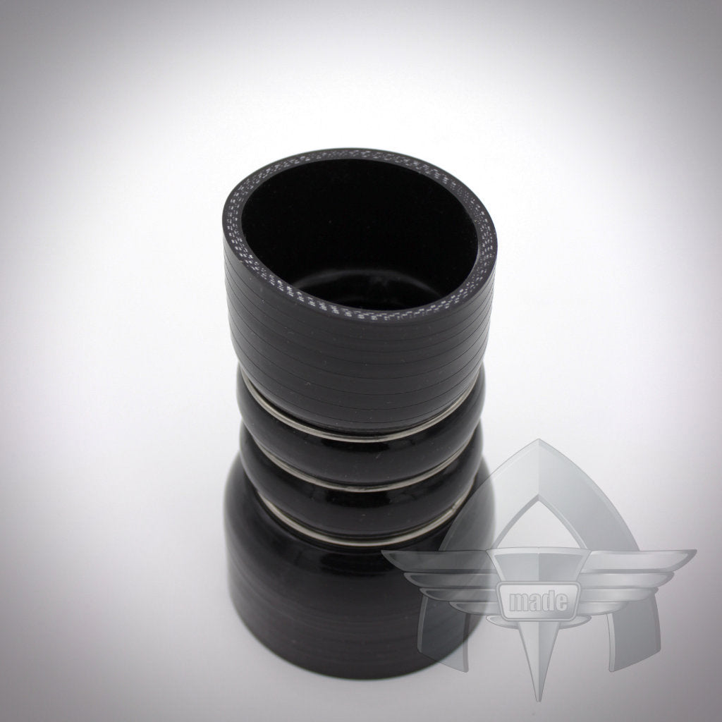 Schwarzer, zylindrischer Silikonschlauch-Reduzierer mit Rippen, von oben auf weißem Hintergrund dargestellt. Teil des ATmade Custom Silicone Hose Kit Ladeluftverrohrung Exclusive, ideal für FBO-Setups und Ladeluftverrohrungsanwendungen.