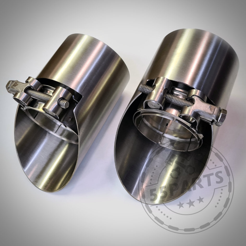 Zwei 55Parts Spezial-Endrohrblenden für F20, F21 M135i aus Edelstahl mit Klemmen, abgeschrägtem Schnitt und reflektierendem Finish liegen auf heller Oberfläche – die perfekte Ergänzung für Ihre Abgasanlage.