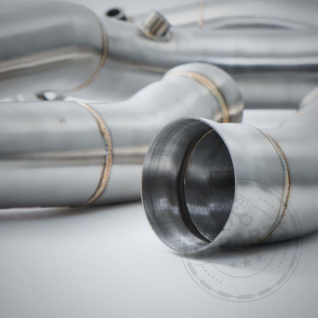 Nahaufnahme der 55Parts High Flow 3,5"-Fallrohre (Katlos oder mit 200 Zeller) für Mercedes Benz AMG C63(S) W205 M177. Zu sehen sind Edelstahl-Auspuffrohre und Schweißnähte auf weißem Hintergrund.