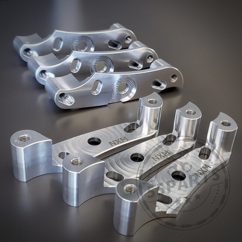 Drei silberne, bearbeitete Metallhalterungen mit mehreren Löchern und eingraviertem Text, angeordnet auf einer dunklen Oberfläche – Teil des Nexsys Motorsport 55Parts Exclusive: NexSys B58 Zündspulen-Upgrade-Kits passend für BMW S55- und N55-Motoren (E8x, E9x, F2x, F3x, F8x).