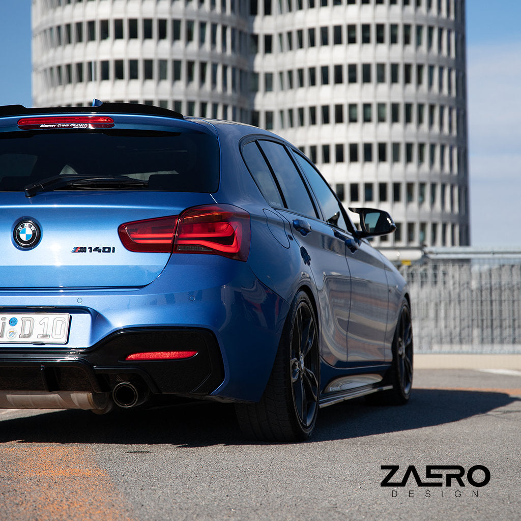 Ein blauer BMW M140i mit Carbon-Anbauteilen und einem ZAERO Evo-1 Diffusor passend für BMW M135i/M140i F2x, glanz schwarz, parkt in einer Stadtstraße mit hohen, runden Gebäuden. Das ZAERO-Logo ist in der Szene sichtbar.