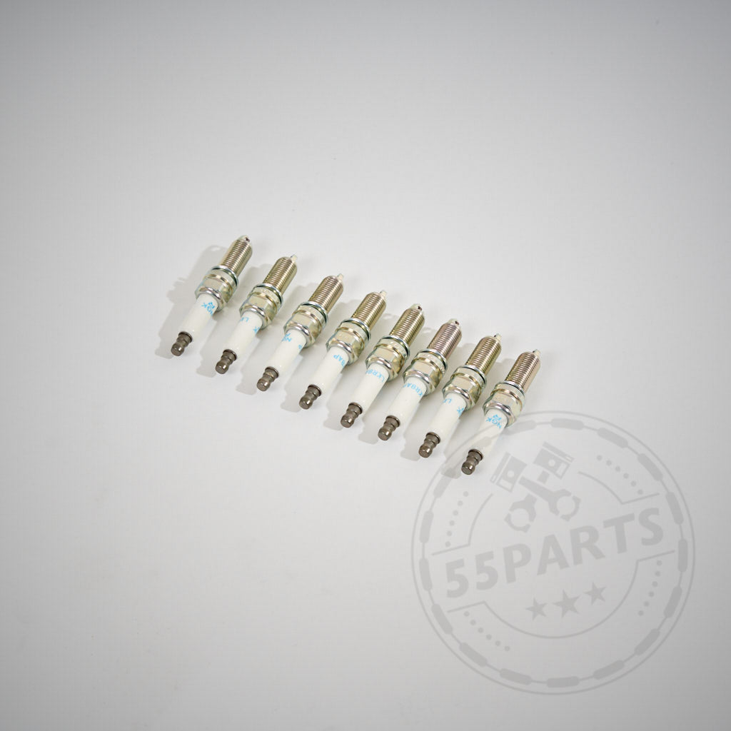 Acht NGK-Zündkerzen für den BMW E9x M3 S65-Motor, in einer Reihe auf einer weißen Fläche angeordnet, mit einem schwachen 55Parts-Logo in der Ecke.