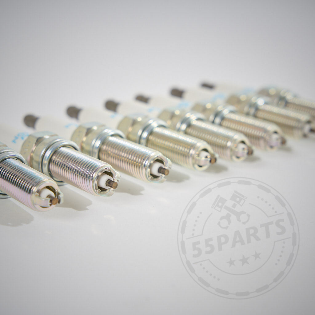 Acht NGK-Zündkerzen passend für BMW E9x M3 mit S65-Motor, in einer Reihe auf einer weißen Oberfläche angeordnet; mit schwachem 55Parts-Wasserzeichen.