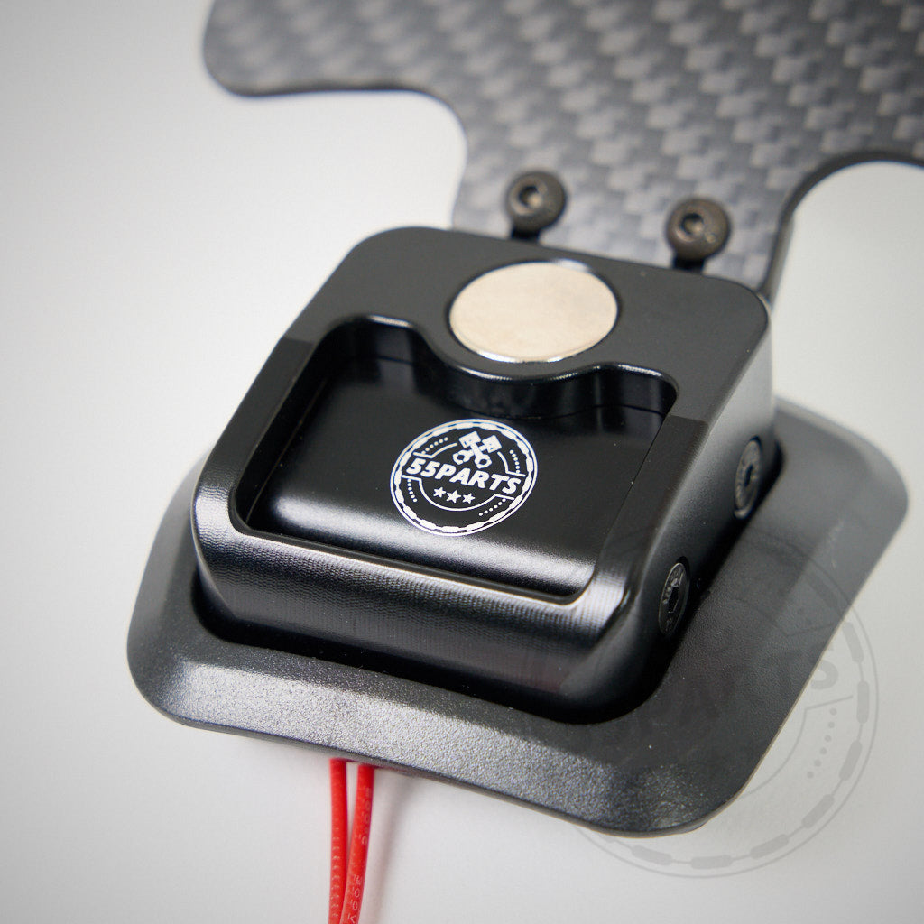 Nahaufnahme eines 55Parts-Specials: Magnetischer Schaltwippenschalter V2 passend für BMW E9X M3 mit dem „55Parts“-Logo auf einer Kohlefaseroberfläche.