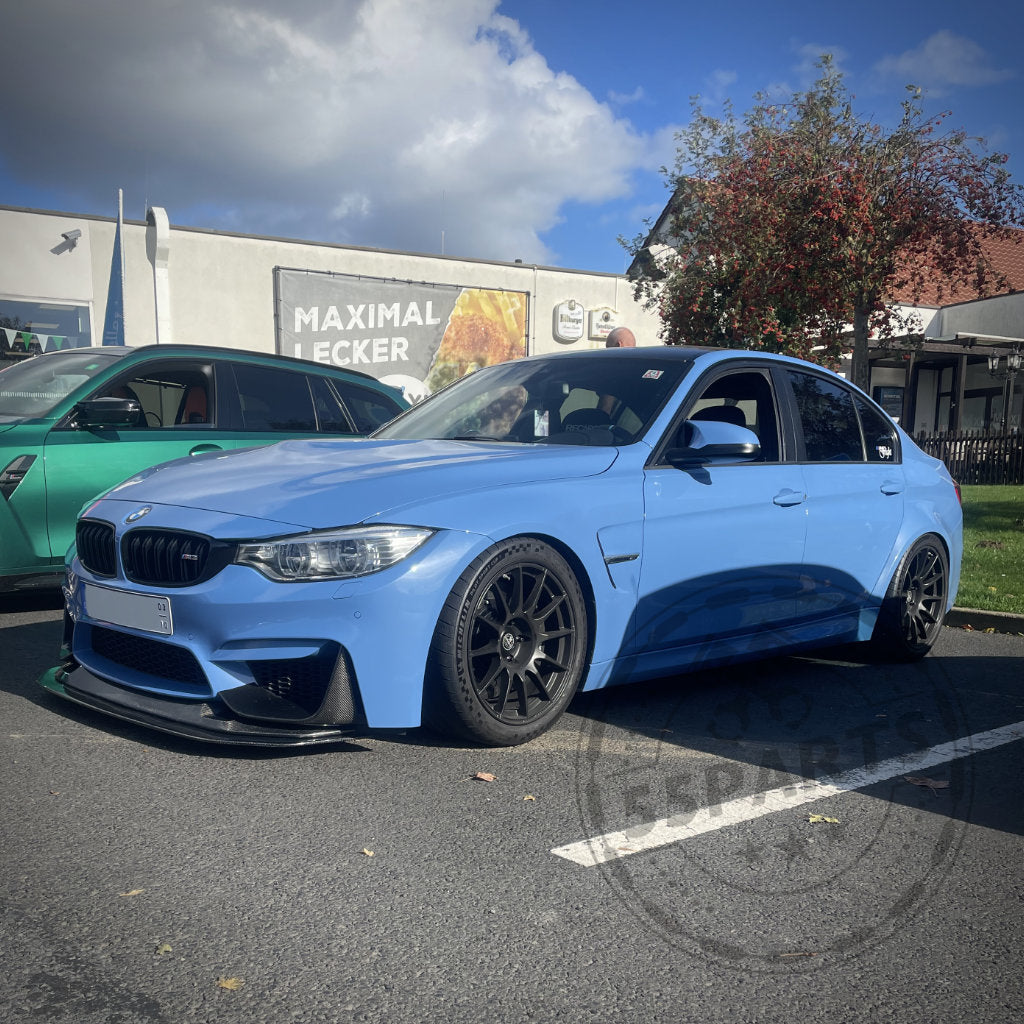 An einem sonnigen Tag steht auf einem Parkplatz ein blauer BMW-Sportwagen mit schwarzen Rädern. Für eine verbesserte Optik sind spezielle CNC-gefräste Radkappen für ProTrack One-Räder angebracht.