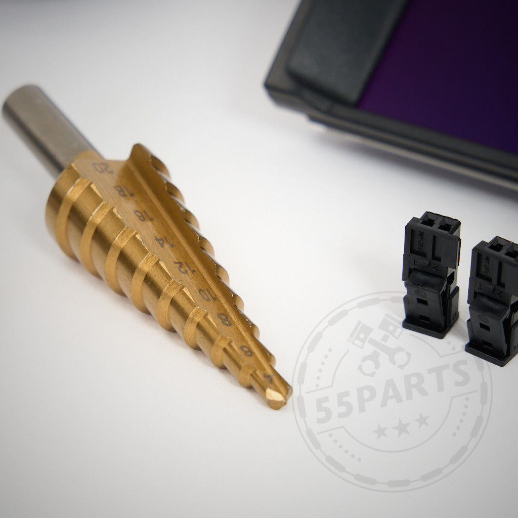 Ein Stufenbohrer und zwei schwarze Kunststoffverbinder liegen auf einer weißen Oberfläche neben einem AK Motion DataDisplay NextGEN passend für BMW Modelle-Gerät von AK Motion.