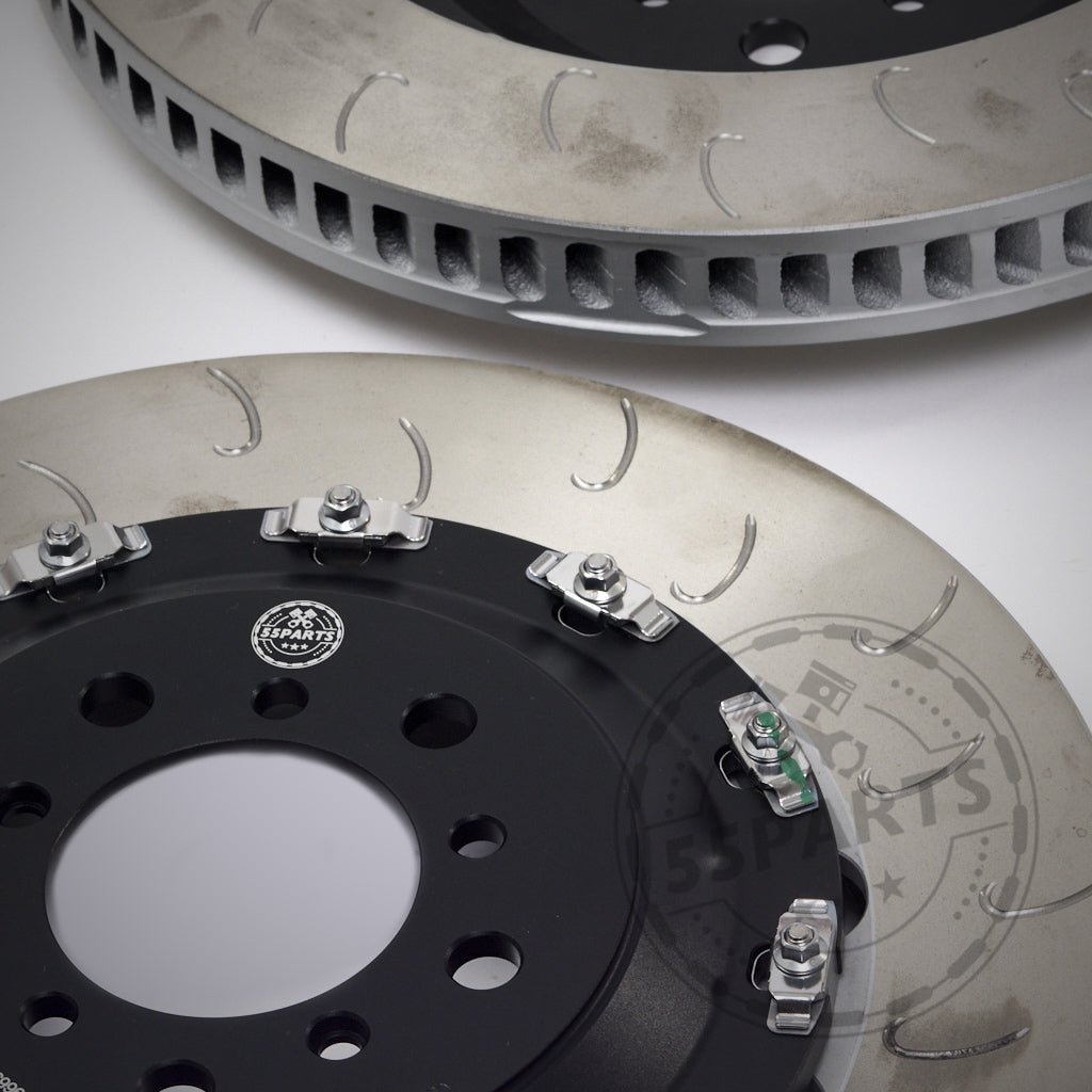 Nahaufnahme von zwei nachträglich belüfteten Schlitzrotoren mit angebrachter Hardware des 55Parts Special: AP Racing Big Brake Kit, ausgestellt auf einer hellen Oberfläche.