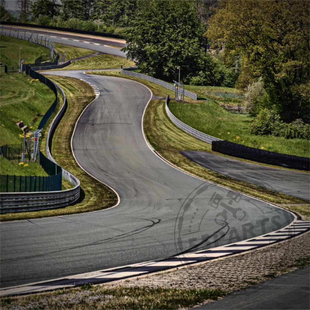 Eine kurvenreiche Rennstrecke schlängelt sich unter einem strahlend sonnigen Himmel durch üppiges, grasbewachsenes Gelände und bietet ein aufregendes Rennerlebnis.