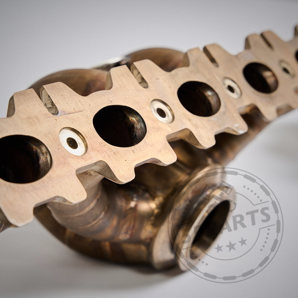 Nahaufnahme des 55Parts Special Big Turbo Kit 1000PS B58 Gen. 1 für die Serien F2X, F3X, G3X, G01, G02; metallischer Krümmer mit sechs runden Anschlüssen und Schweißverbindungen, ideal für Turboanwendungen.