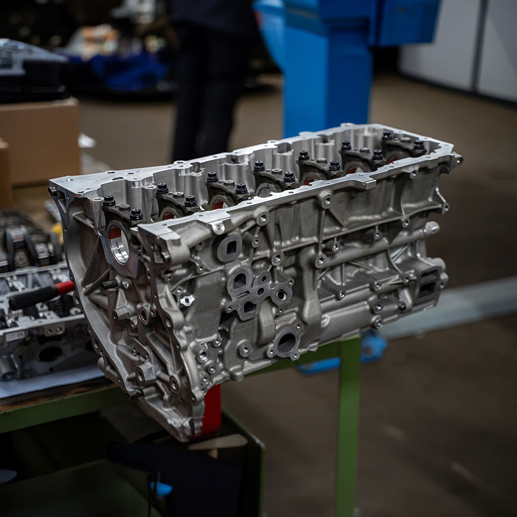 Ein metallischer Motorblock steht auf einer grünen Werkbank in einer Industriewerkstatt, umgeben von Präzisionswerkzeugen.