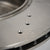 Nahaufnahme eines 55Parts Spezial-Montagesatzes (Bremsscheiben und Buchsen) zur Montage von 2-Kolben-Performance-Bremssätteln an BMW E8x/E9x-Modellen, mit drei Bohrlöchern und einem teilweise sichtbaren Logo im Hintergrund.