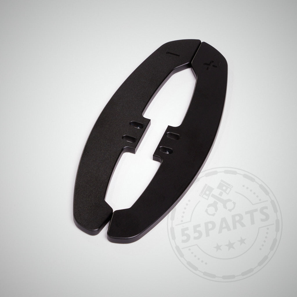 Schwarze, ovale 55Parts Special CNC-Aluminium-Paddel für magnetische Schaltwippen, mit Plus- und Minus-Symbolen auf hellem Hintergrund.