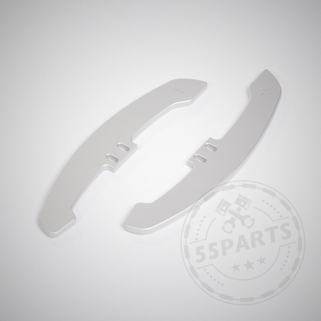 Zwei silberne 55Parts Special CNC-gefräste Aluminium-Paddles für magnetische Schaltwippen/Magnetic Paddle Shifter ruhen auf einer weißen Oberfläche, mit einem schwachen 55Parts-Logo-Wasserzeichen.