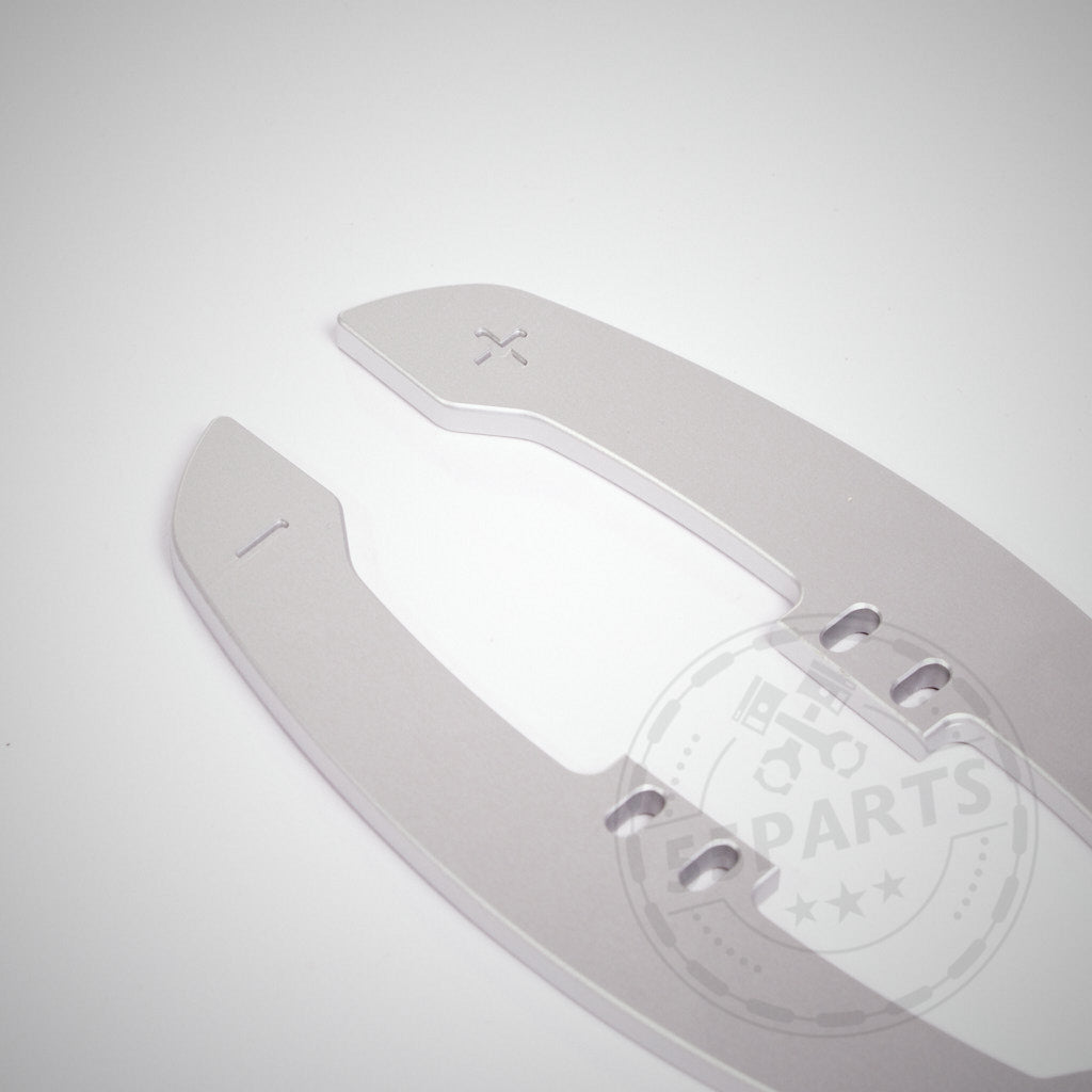 CNC-gefrästes silbernes Aluminiumpaddel mit Aussparungen und eingravierten Plus-/Minuszeichen, konzipiert für die Verwendung mit 55Parts Special: Magnetische Schaltwippen / Magnetic Paddle Shifter, abgebildet auf einem schlichten weißen Hintergrund.