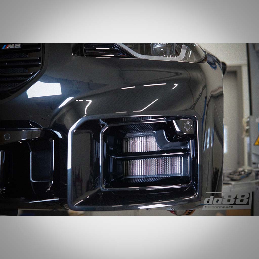Nahaufnahme einer schwarzen Frontstoßstange eines BMW M2 mit dem Aluminium-Upgrade-Kühlmittelkühler von do88, dem modernen seitlich montierten Kühler passend für BMW G87 M2, G80 G81 M3 und G82 G83 M4 S58.
