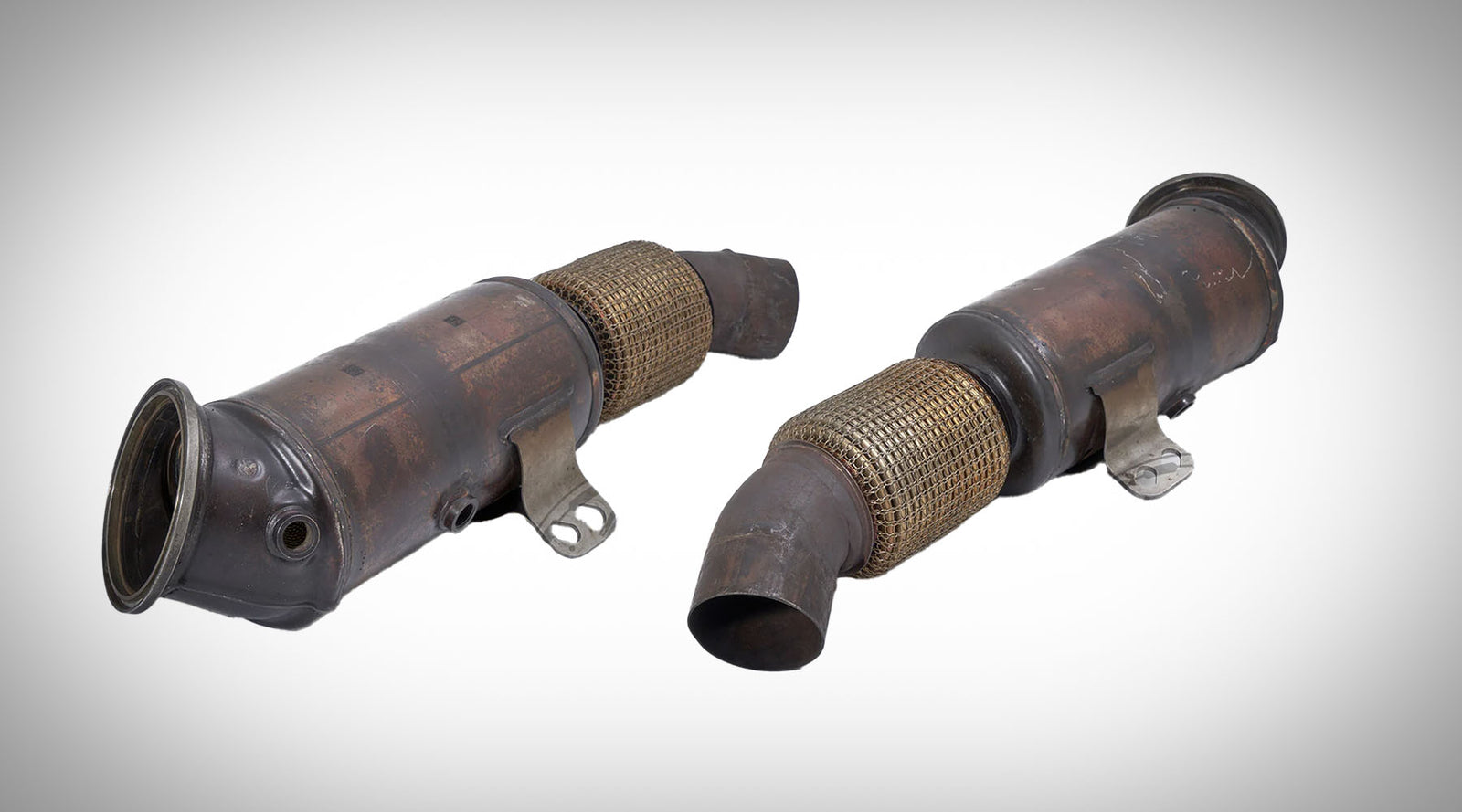 Zwei gebrauchte Autokatalysatoren mit Metallgitter und abgewinkelten Rohren, auf weißem Hintergrund dargestellt, ideal für die Reparatur von Fahrzeugabgassystemen.