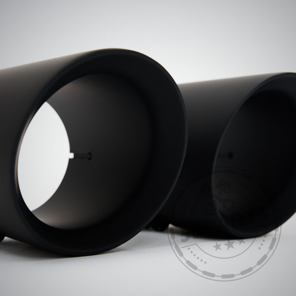 Zwei schwarze zylindrische 55Parts Special 3" ECE Equal Length Abgasanlage-Endschalldämpfer, entwickelt passend für BMW F8x M2 Competition, M3 und M4 (alle Modelle), sind nebeneinander auf einer weißen Fläche platziert.