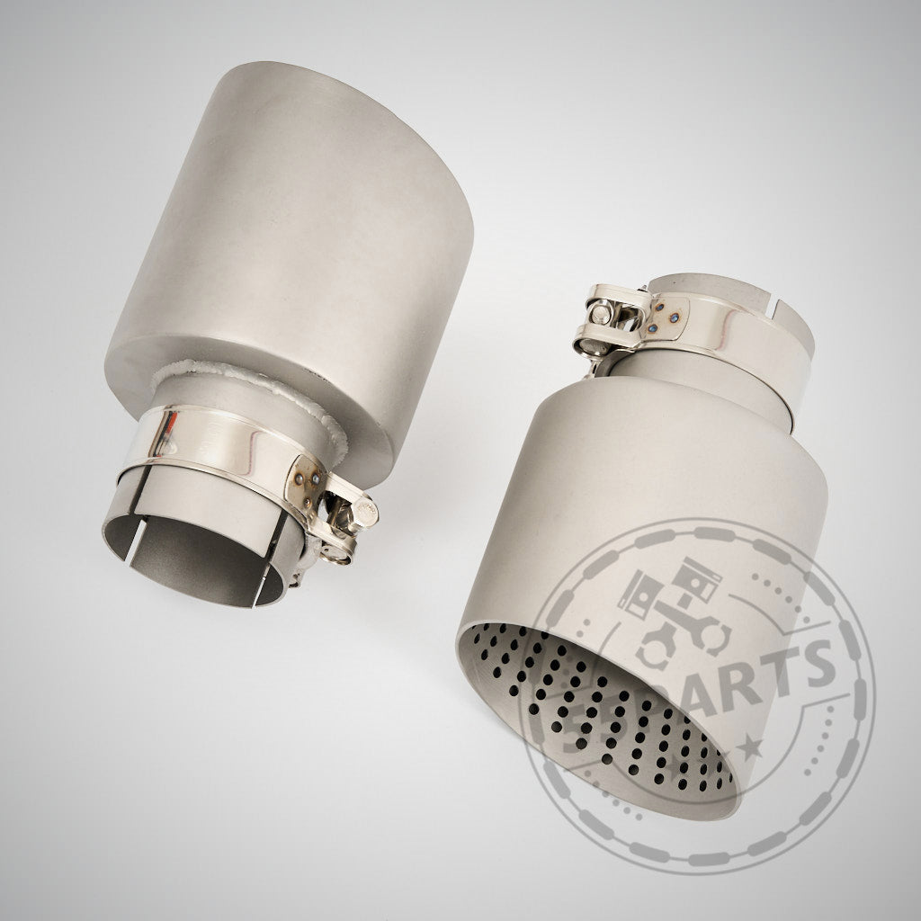 Zwei metallische Auspuffblenden mit Schellen – eine geschlitzt, eine gelocht – für die 55Parts Special 3" ECE Abgasanlage, kompatibel mit BMW G8x Modellen (G81, G82, G83, G87 M2/M3/M4 Competition) mit S58 Motor. Heller Hintergrund.