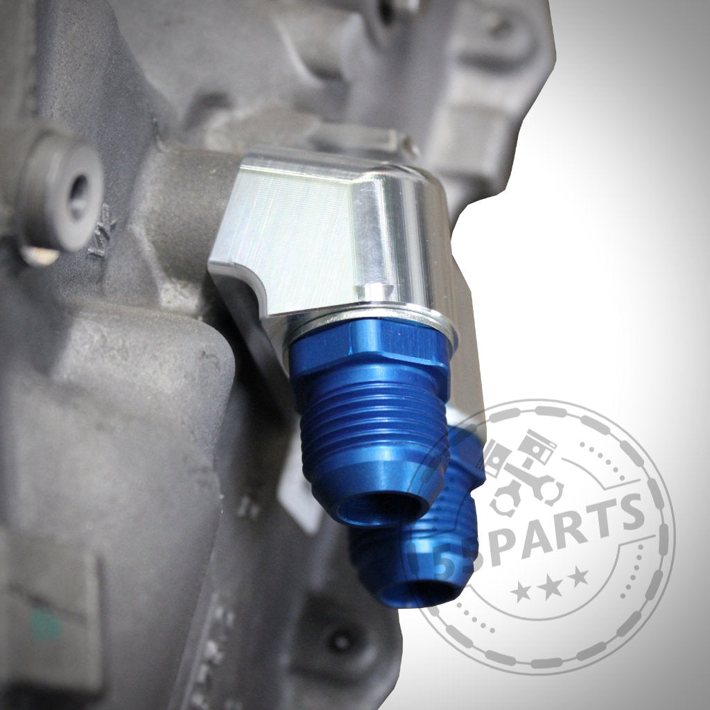 Nahaufnahme eines blau eloxierten 55Parts-Exklusiv-Ölkühleradapters für ZF 8HP50 und 8HP70 Dash10, der an einem metallischen Autobauteil befestigt ist, mit einem verblassten 55Parts-Logo in der Ecke.