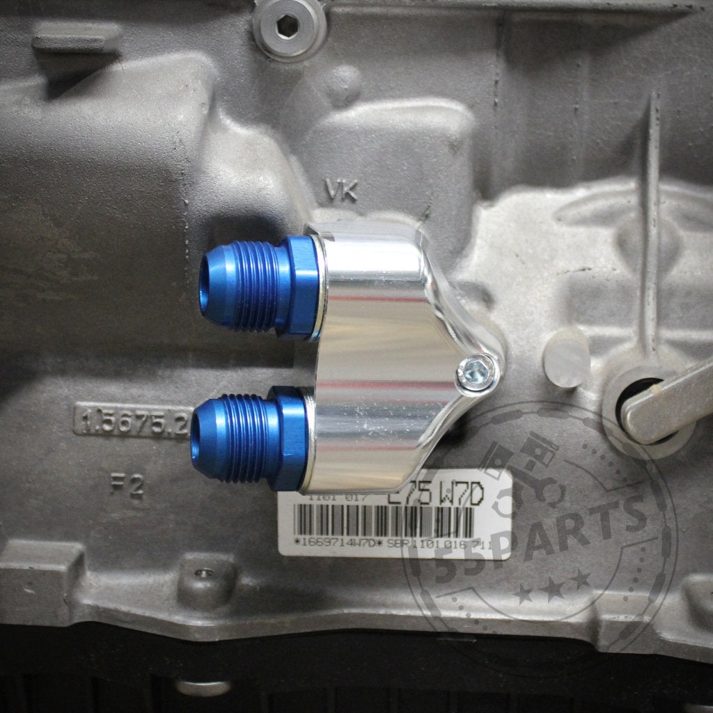 Nahaufnahme des 55Parts Exclusive: Ölkühleradapters für ZF 8HP50 und 8HP70 Dash10, mit zwei blauen Armaturen an einem grauen BMW Motoren-Motor und der Hervorhebung seiner wesentlichen Rolle im Kühlsystem.