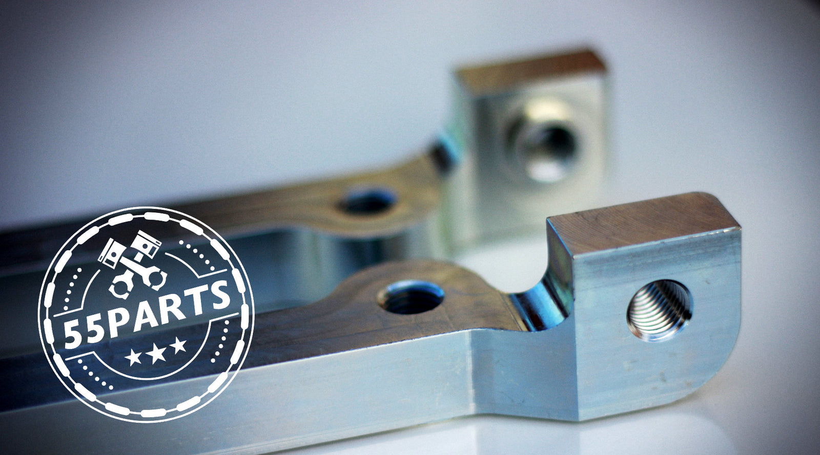 Zwei bearbeitete Metallteile mit Löchern, versehen mit einem 55PARTS-Logo mit Kolben und Sternen.