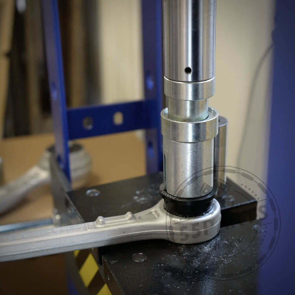 Ein Metallwerkzeug presst mithilfe einer hydraulischen Presse ein Teil, wobei zur zusätzlichen Unterstützung ein Schraubenschlüssel darunter angebracht ist.