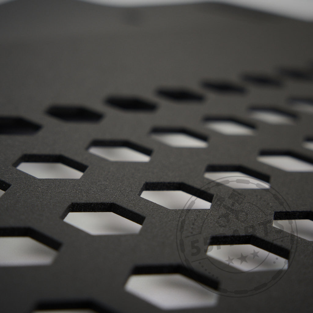 Nahaufnahme des 55Parts Skid Plate Ölkühler Schutz passend für BMW M2, M3, M4 (G80/G81/G82/G83/G87) mit einer schwarzen Oberfläche mit sechseckigen Ausschnitten in einem geometrischen Muster.