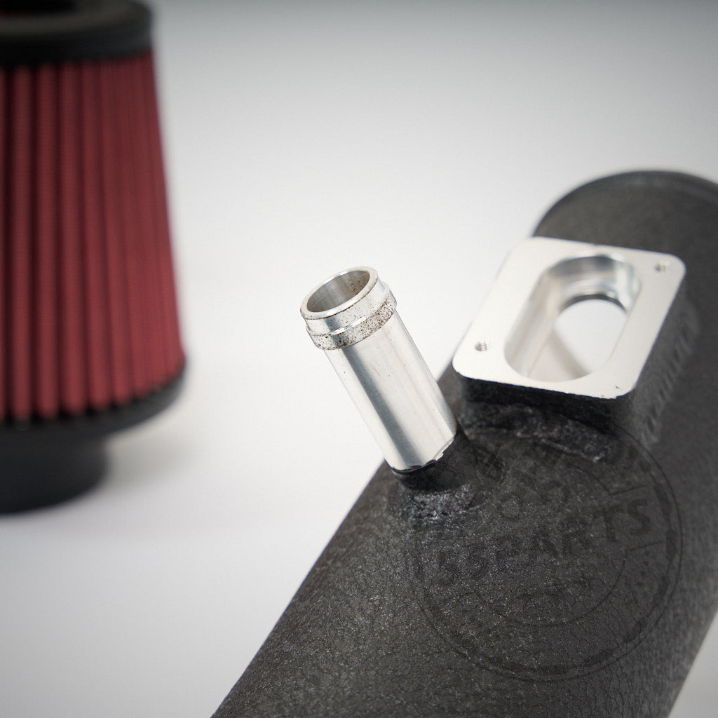 Nahaufnahme eines schwarzen Ansaugrohrs mit Metallfitting aus dem 55Parts Special offene Ansaugung passend für BMW 1er F2x, 2er F2x, 3er F3x, 4er F3x, M2 F87 N55; roter Luftfilter unscharf im Hintergrund.