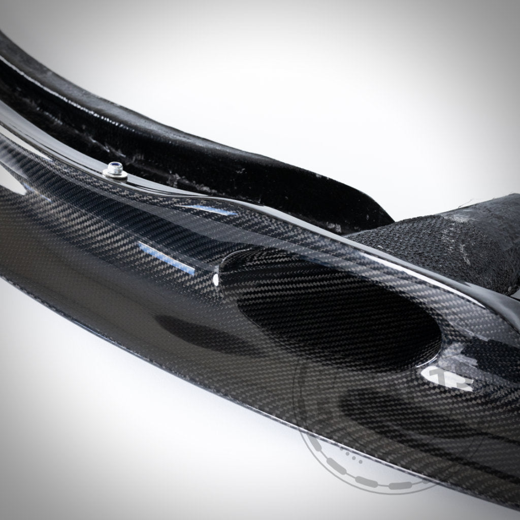 Nahaufnahme des 55Parts Echtcarbon-Frontschwerts Frontlippe GT4 mit Bremsbelüftung, passend für BMW E9x M3, das sein glänzendes Carbon-Finish, die aerodynamisch geschwungene Form und die integrierten Bremskühlkanäle zeigt.