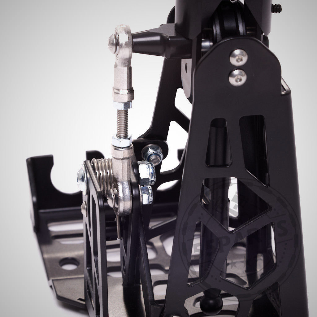 Nahaufnahme des HRE Shortshifter &amp; HRE, einer mechanischen Pedalbaugruppe aus schwarzem Metall mit Schrauben und Federn, die speziell für den GR Yaris entwickelt wurde und vor einem hellen Hintergrund zu sehen ist.