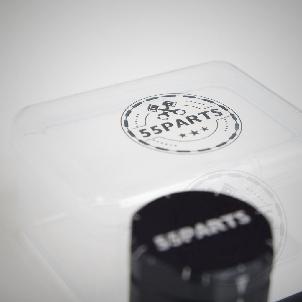 Durchsichtiger Kunststoffbehälter und schwarzes zylindrisches Werkzeug, beide mit der Aufschrift 55Parts, auf weißem Hintergrund. Dieses 55Parts Kit enthält eine magnetische Zündkerzennuss und ein Biegewerkzeug, ideal für BMW Zündkerzenwechsel und Service.