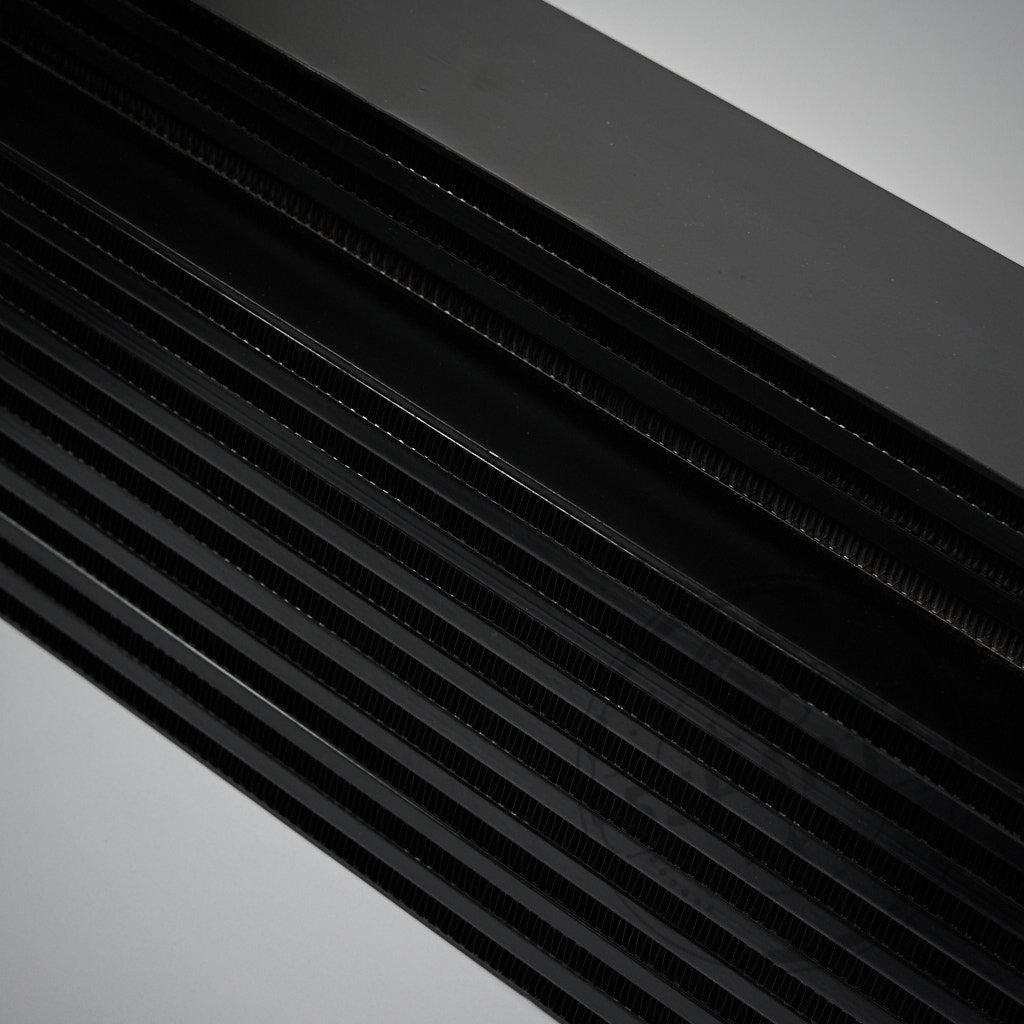 Nahaufnahme der gestapelten schwarzen Metalllamellen vom 55Parts-Exklusivangebot: Upgrade-Ladeluftkühler passend für Toyota GR Yaris,, auf grauem Hintergrund.