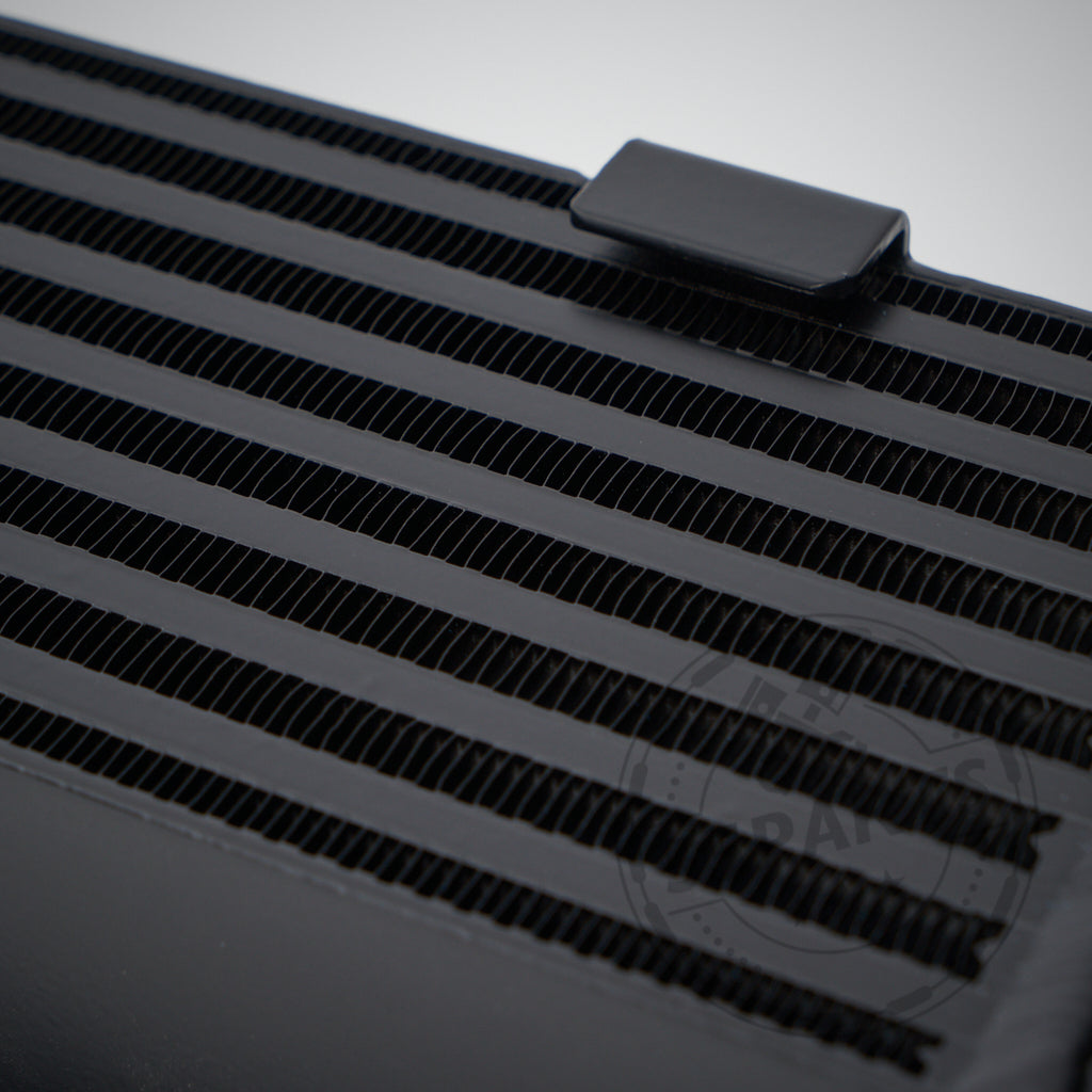 Nahaufnahme eines schwarzen 55Parts Upgrade-Ladeluftkühlers aus Metall mit horizontalen Kühlrippen, passend für die Modelle BMW 325d, 330d und 335d M57.