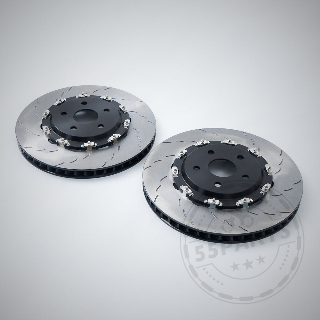 Two 55Parts Carbopad zweigeteilte, schwimmend gelagerte Bremsscheiben (380mm) passend für BMW M2, M3, M4 F8x mit schwarzen Zentren liegen nebeneinander auf hellgrauem Hintergrund.