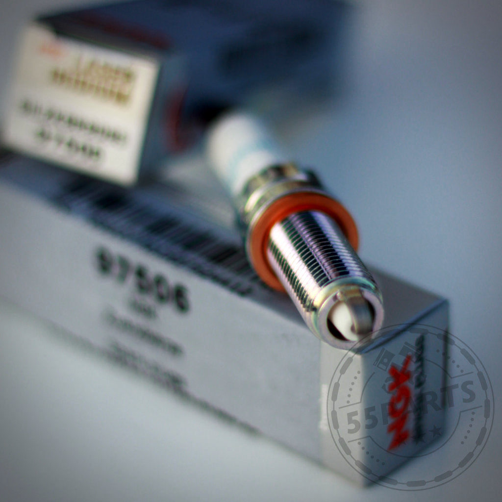 Nahaufnahme eines NGK Zündkerzen-Sets 97506 (SILZKBR8D8S) auf seiner Verpackung, mit einem weiteren unscharfen NGK Zündkerzen-Set im Hintergrund.